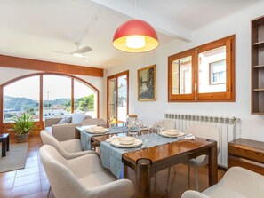 A dining area with a table set for four, a ceiling fan, and a large window with a view of the countryside.