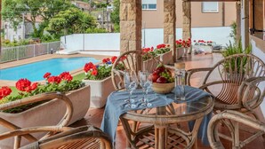 A covered outdoor dining area with wicker chairs, a pool, and red flowers. - Beautiful private villa for 8 people with WIFI, private pool, TV, terrace and panoramic view (Tordera)