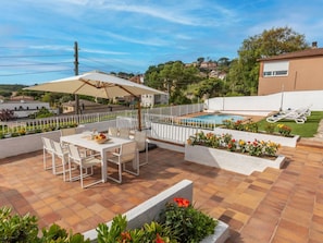 Une terrasse avec une table et des chaises, une piscine et une clôture blanche.
