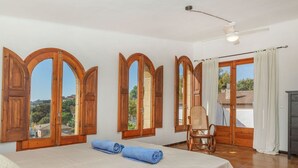 A room with a bed, a chair, wooden-framed windows, a ceiling fan, and a view of the outside. - Beautiful private villa for 8 people with WIFI, private pool, TV, terrace and panoramic view (Tordera)