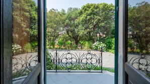 Blick durch eine Glastür auf einen Balkon mit Metallgeländer, umgeben von üppigem Grün und Bäumen.