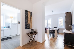 A modern kitchen with white cabinets, a dining area with a table and chairs, and a living room with a sofa and a large window.