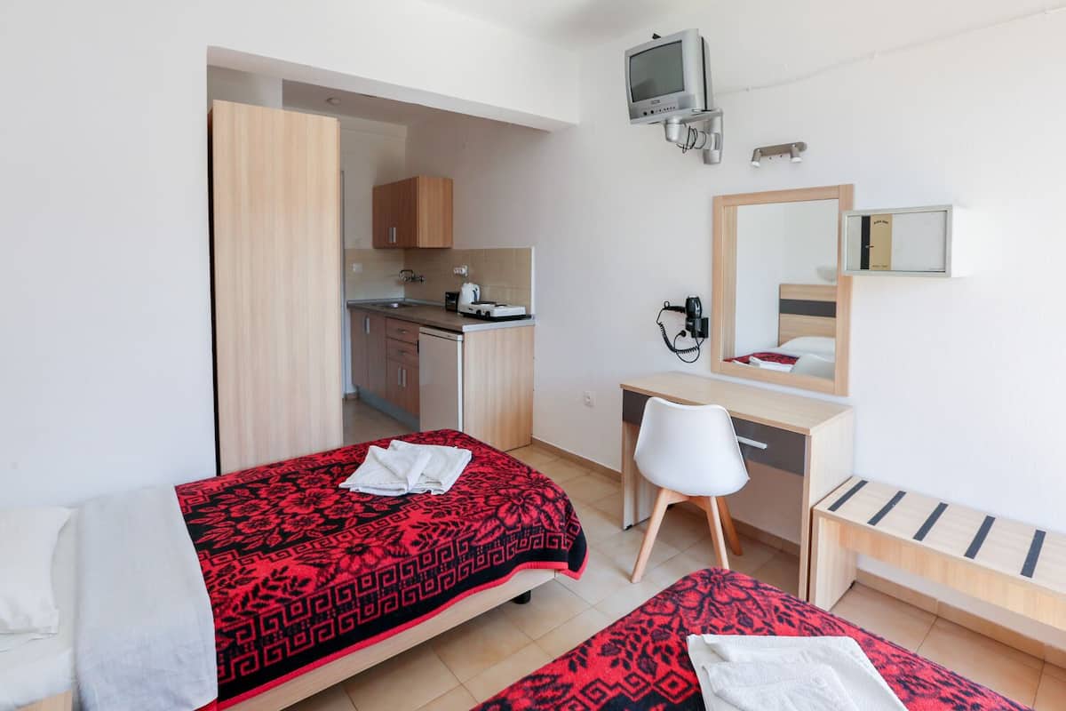 A hotel room with two beds, a desk, a chair, a TV, a mirror, and a kitchenette.