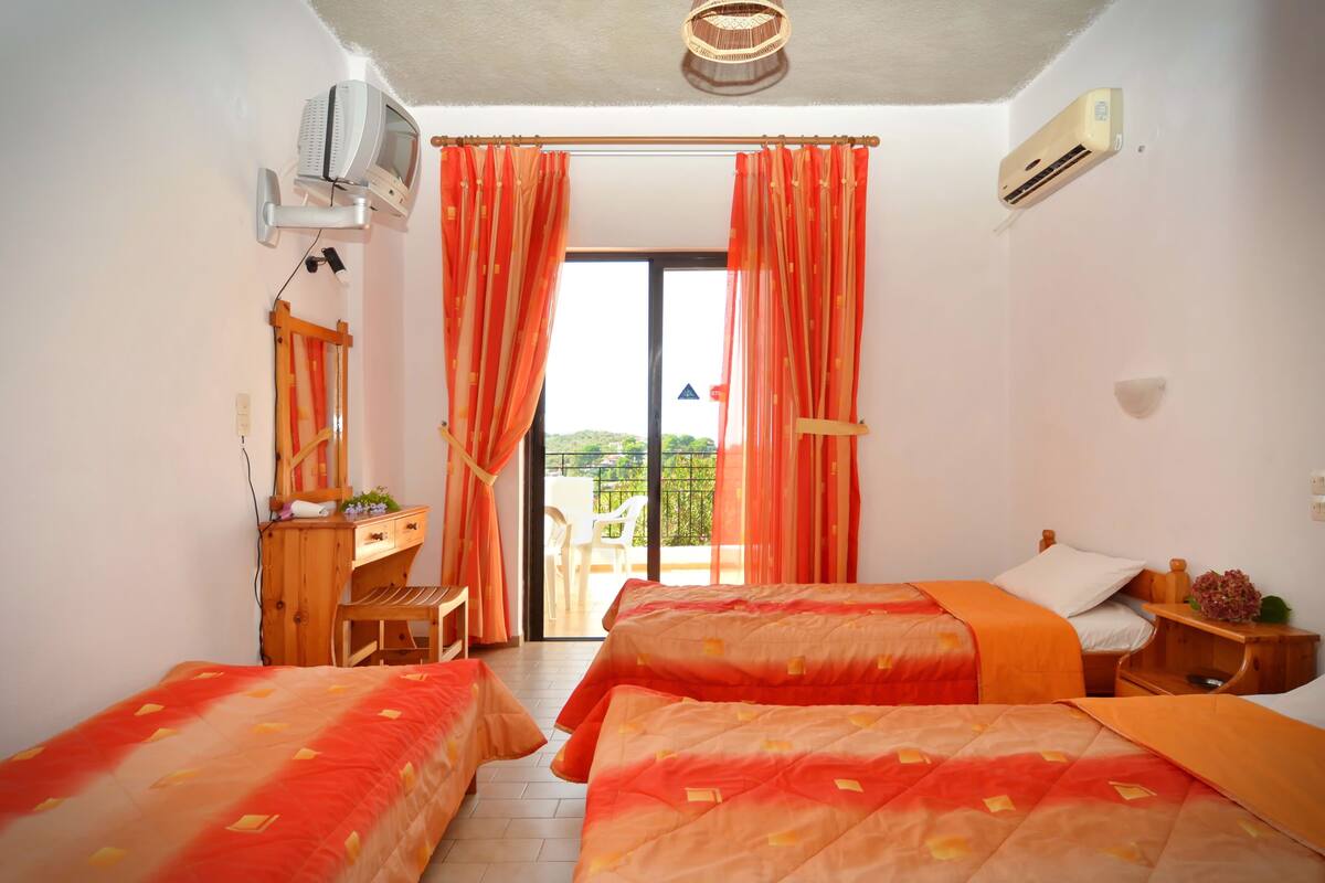 A hotel room with two beds, a desk, a chair, an air conditioner, and a view of the outdoors.