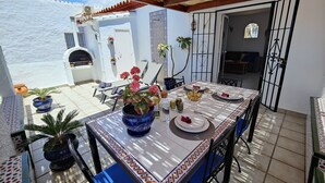 A sunlit patio with a table set for dining, potted plants, and a view of the sea. - AP327 - Casa Pico (Nerja)