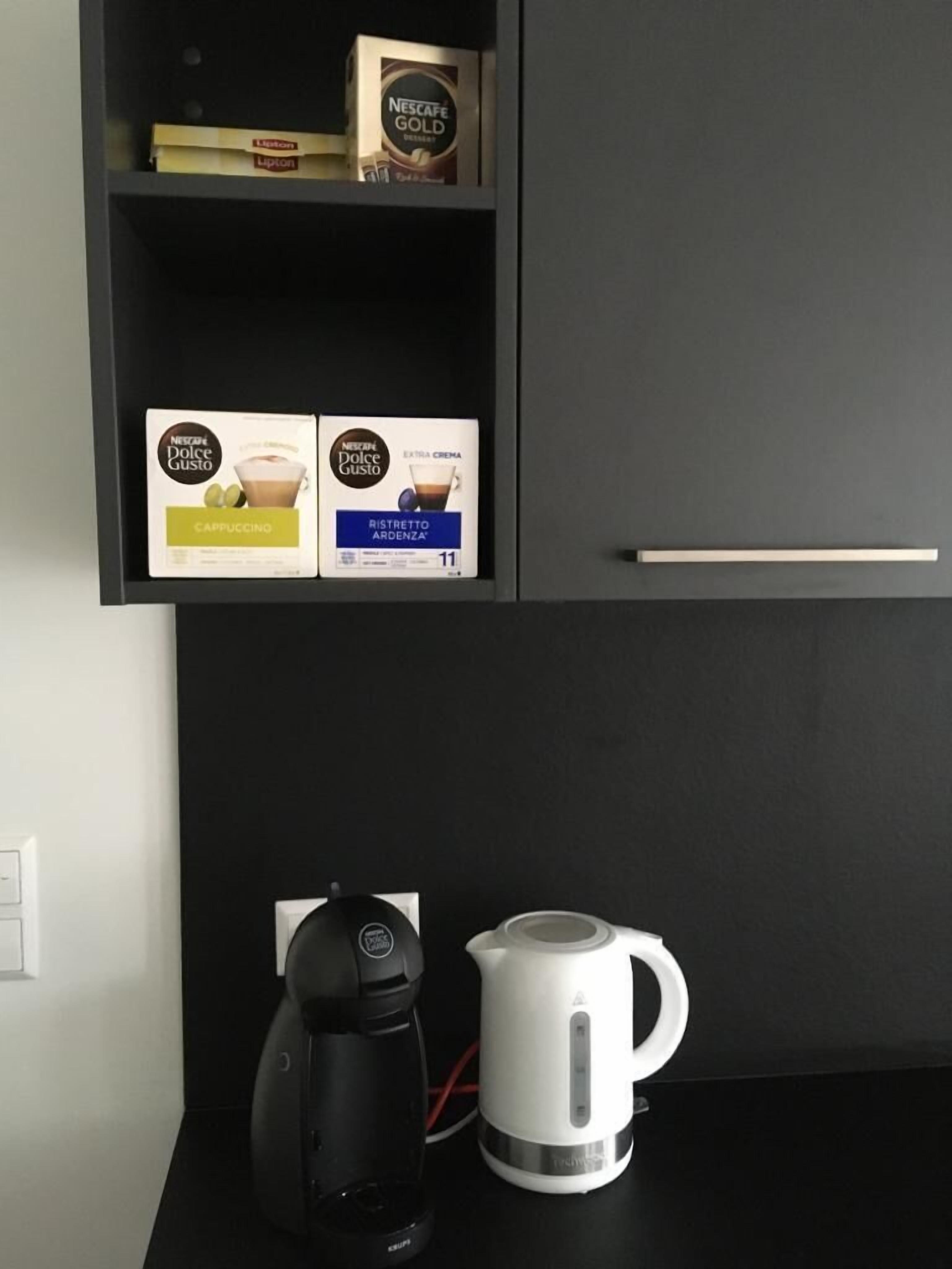 Een zwart schap met Nescafe Dolce Gusto koffiecups en een zwarte koffiemachine op een zwart aanrecht.