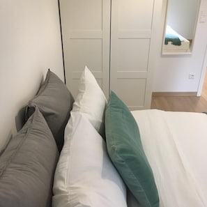 A bed with pillows in a room with a wooden floor and a white door.