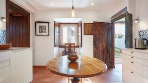 A kitchen with a round wooden table, white cabinets, a hanging light fixture, and a window with an open door.