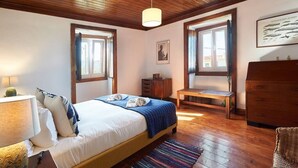 A bedroom with a wooden ceiling, a bed with a blue blanket, a wooden bench, and a dresser.