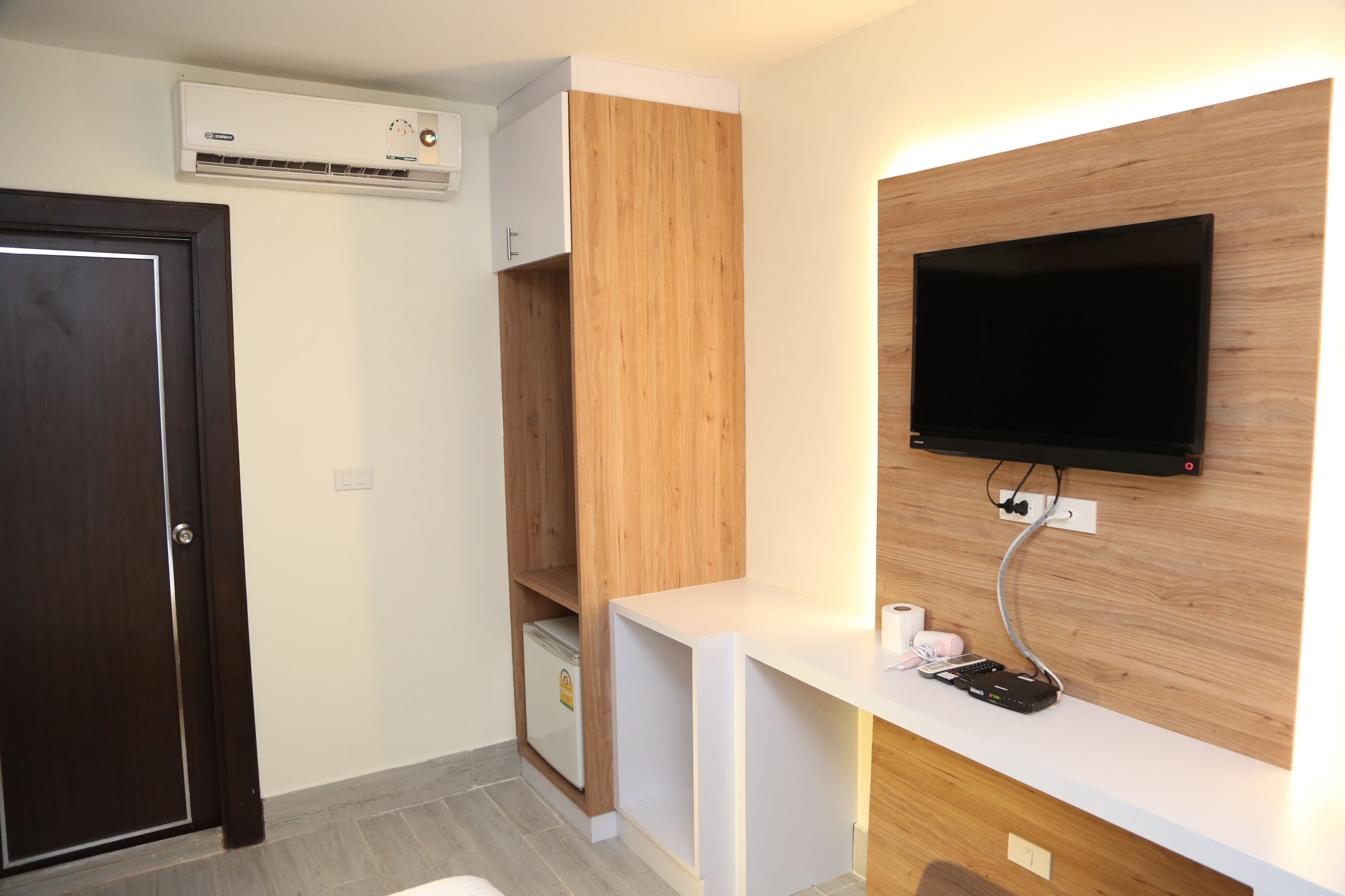 A modern room with a wooden cabinet, a white desk, a mounted TV, and an air conditioning unit.