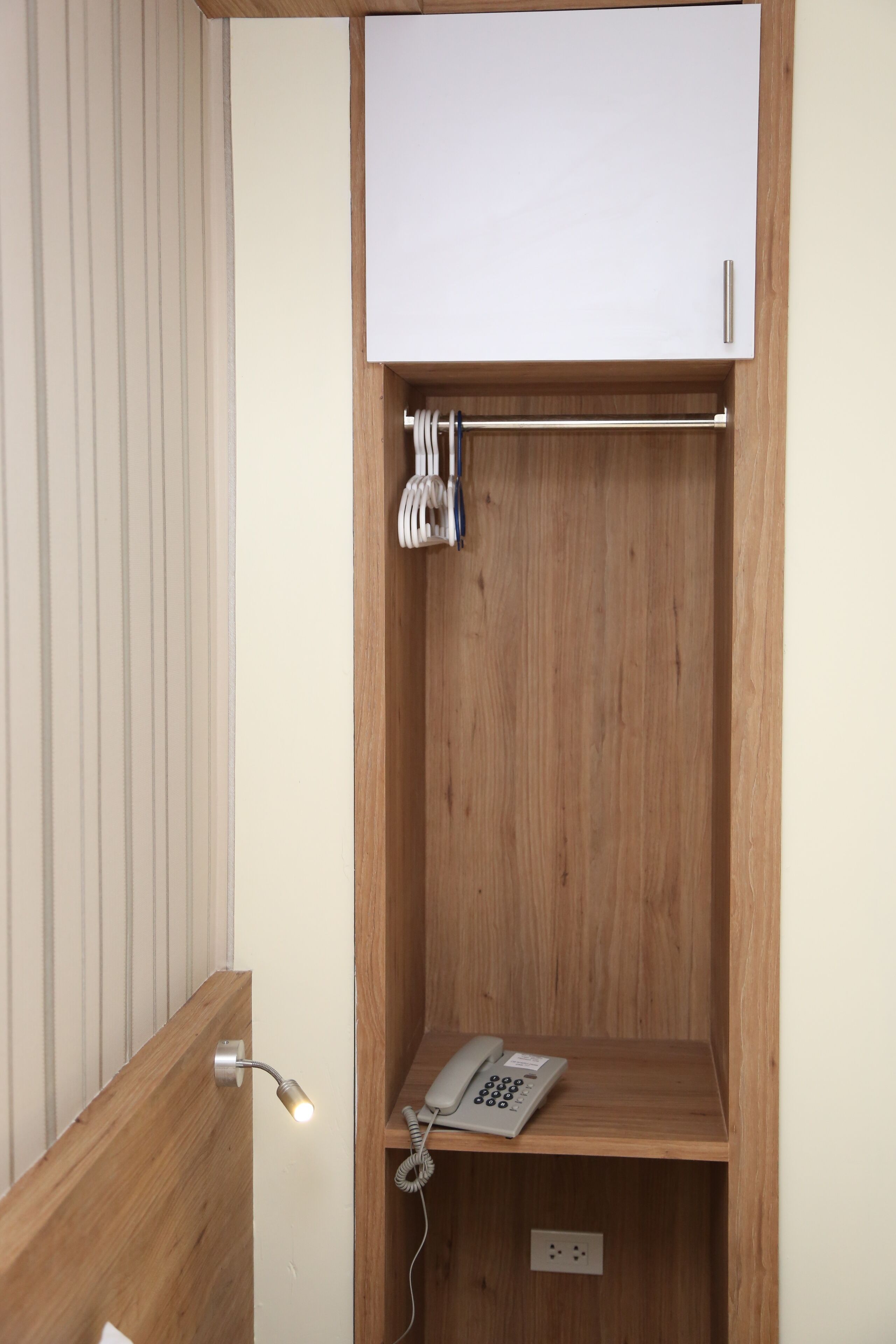A wooden cabinet with a white door, a telephone, and a coiled cable.