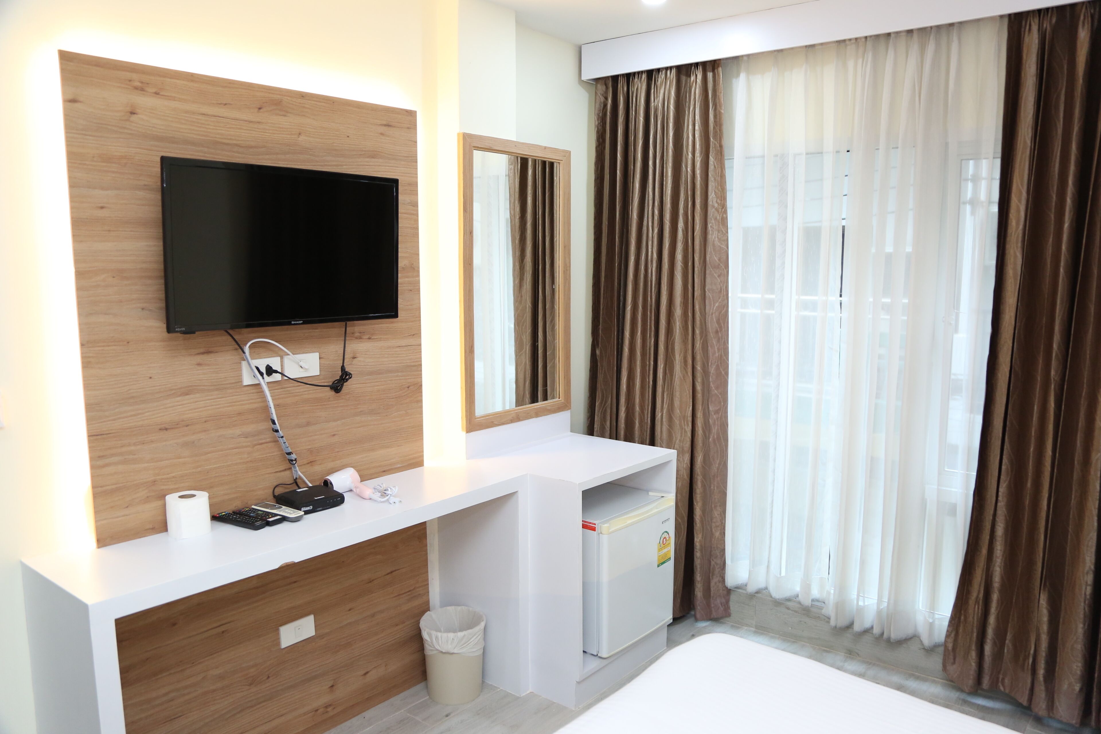 A modern bathroom with a wooden vanity, a mounted TV, a mirror, and a window with curtains.