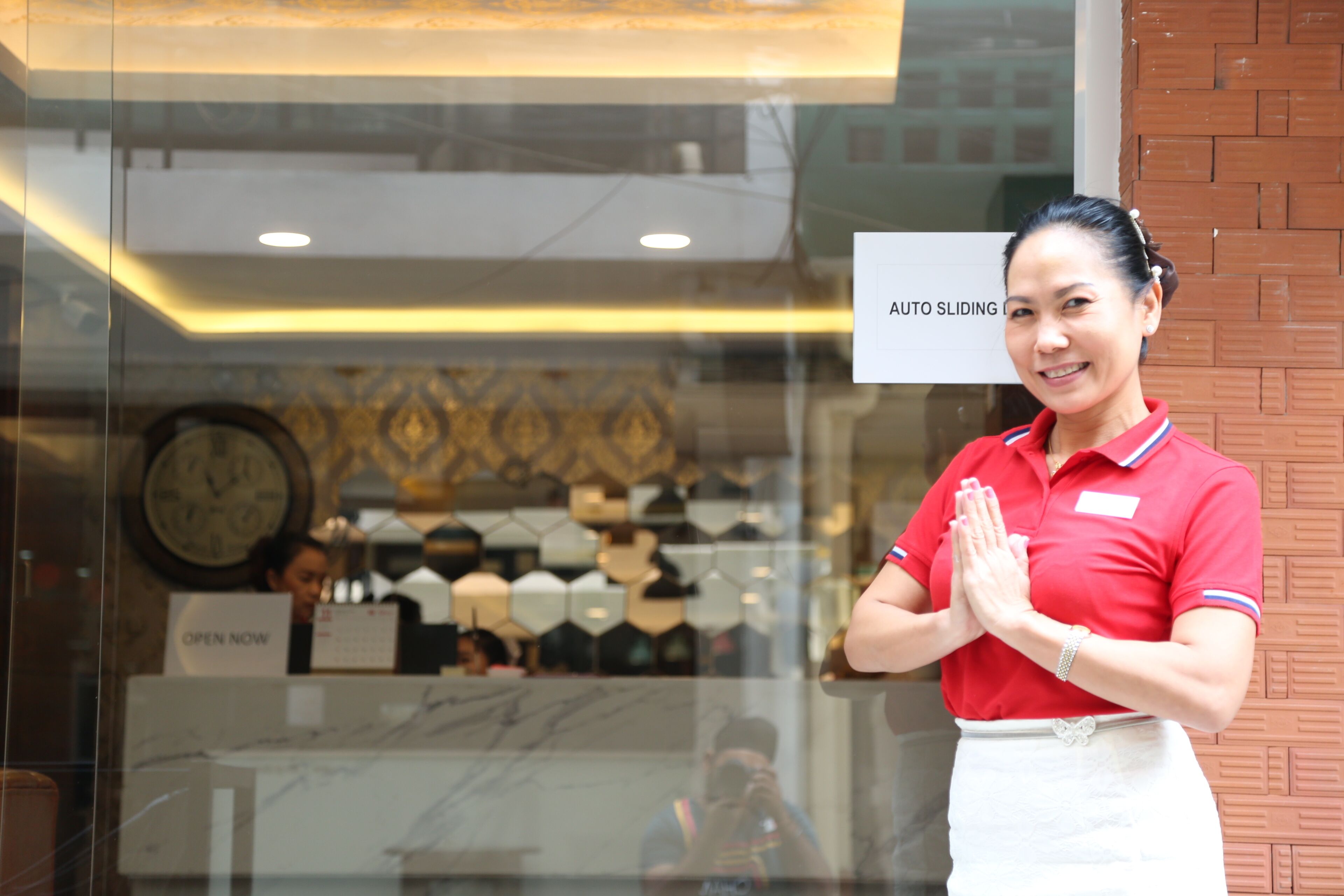 Een vrouw in een rood uniform staat voor een glazen deur met een bord waarop staat 'AUTO SLIDING DOOR'.