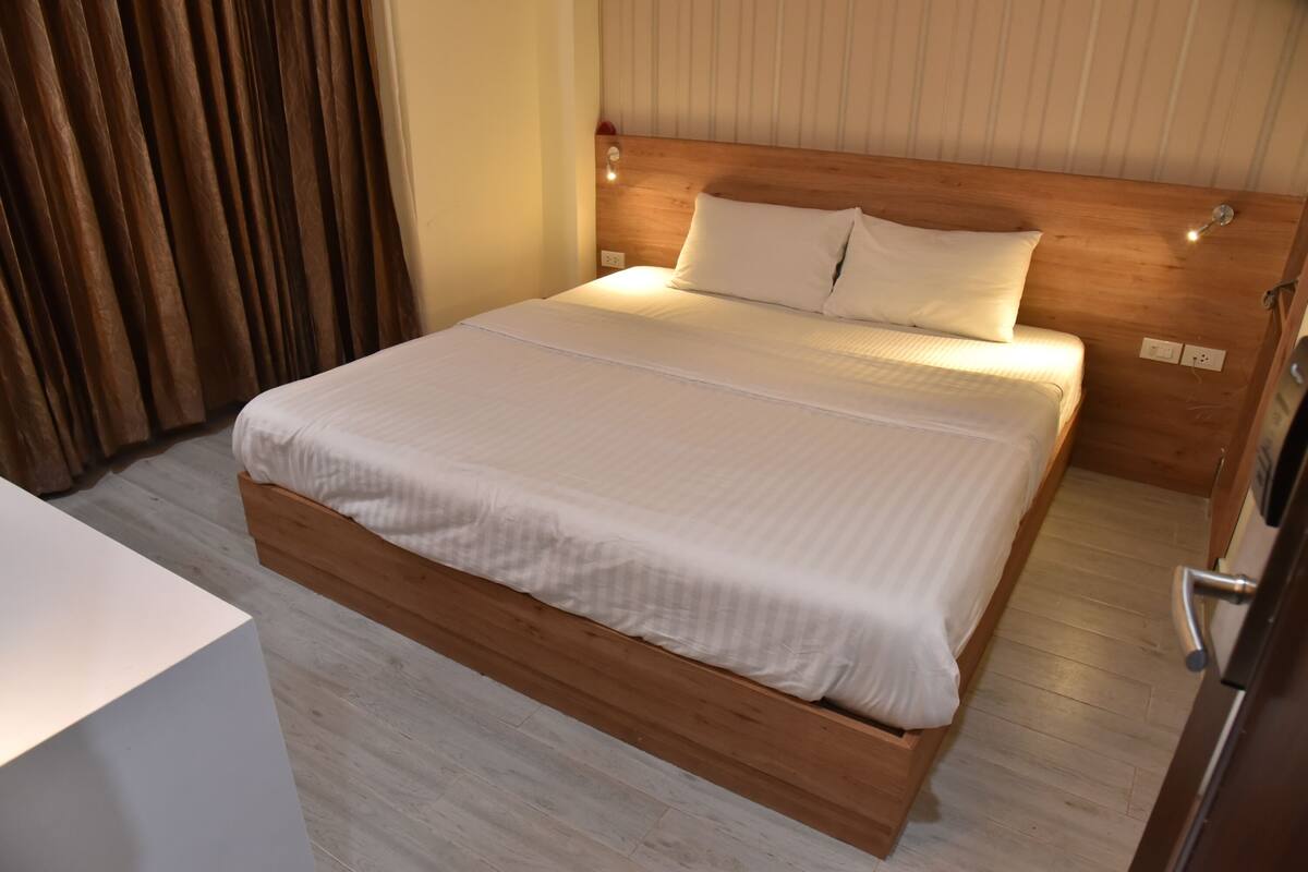 A neatly made bed with a wooden headboard, a bedside table, and a wooden floor.