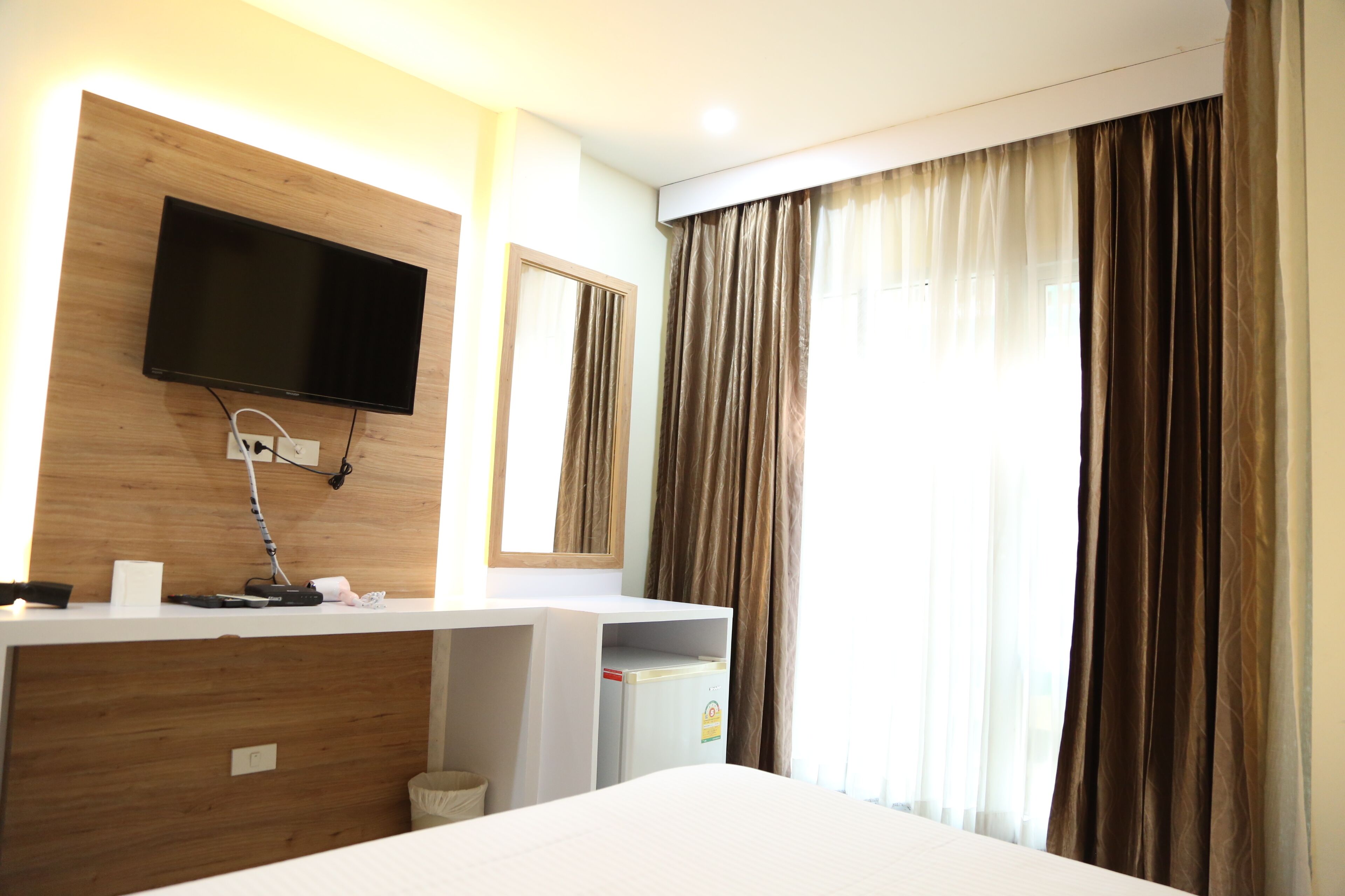 Habitación de hotel con televisor de pantalla plana en una pared de madera, un pequeño escritorio con teléfono y un minibar.