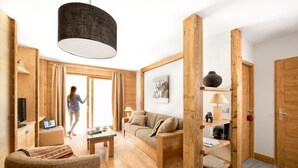 A modern living room with a sofa, coffee table, and a TV. There is a wooden partition with shelves and a lamp. A person is seen walking towards the door. - 100m from ski lifts, fitness, swimming pool, sauna, hammam, balcony, tv, 40m², Tignes (Tignes)