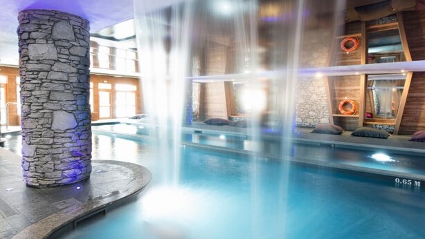 An indoor swimming pool with a stone pillar, a waterfall feature, and a wooden deck area. - 100m from ski lifts, fitness, swimming pool, sauna, hammam, balcony, tv, 40m², Tignes (Tignes)