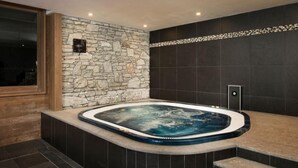 A modern bathroom with a stone wall, a built-in hot tub, and a wooden bench. - 100m from ski lifts, fitness, swimming pool, sauna, hammam, balcony, tv, 40m², Tignes (Tignes)
