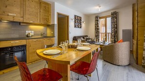 A modern kitchen with wooden cabinets, a dining table set for four, and a cozy living area with a sofa and a fireplace. - 100m from ski lifts, fitness, swimming pool, sauna, hammam, balcony, tv, 40m², Tignes (Tignes)