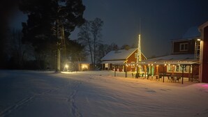A snow-covered landscape with a building featuring a covered outdoor seating area and a lit Christmas tree. - Sjugare Bed & Breakfast (Leksand)