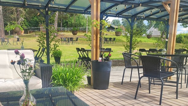 An outdoor patio with a glass-top table, wicker chairs, and a wooden deck. - Sjugare Bed & Breakfast (Leksand)