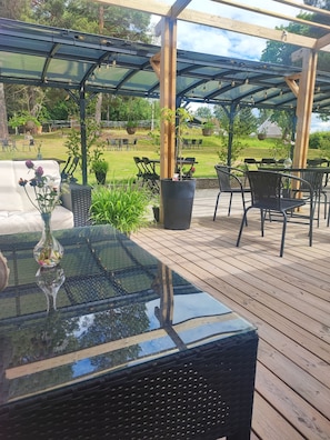Un patio al aire libre con una mesa de vidrio, sillas de mimbre y una terraza de madera.