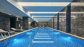 Une piscine intérieure moderne avec un sol carrelé de bleu, des chaises longues et une vue dégagée sur le plafond.