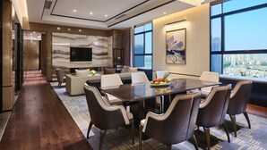 Une chambre d’hôtel moderne offrant une vue imprenable sur la ville, avec un mur en marbre, un téléviseur à écran plat et un coin repas agrémenté d’un panier de fruits.
