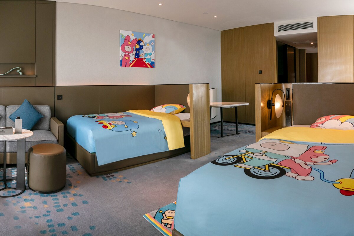 A hotel room with two beds, a desk, and a small seating area.