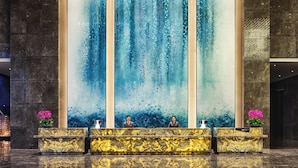 A reception area with marble counters, a large vertical water feature, and two receptionists. - Crowne Plaza Wuhan Development Zone by IHG (Wuhan)