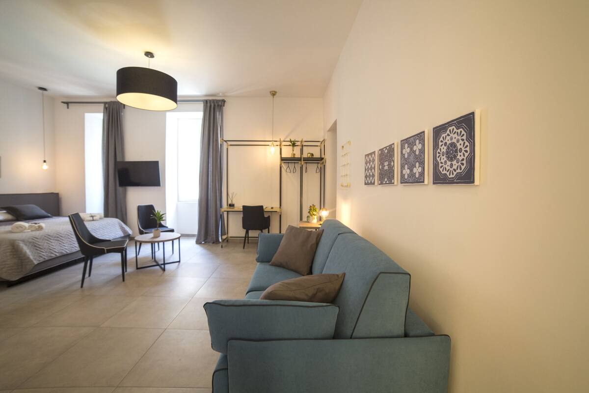 A modern hotel room with a bed, a sofa, a desk, and a TV.