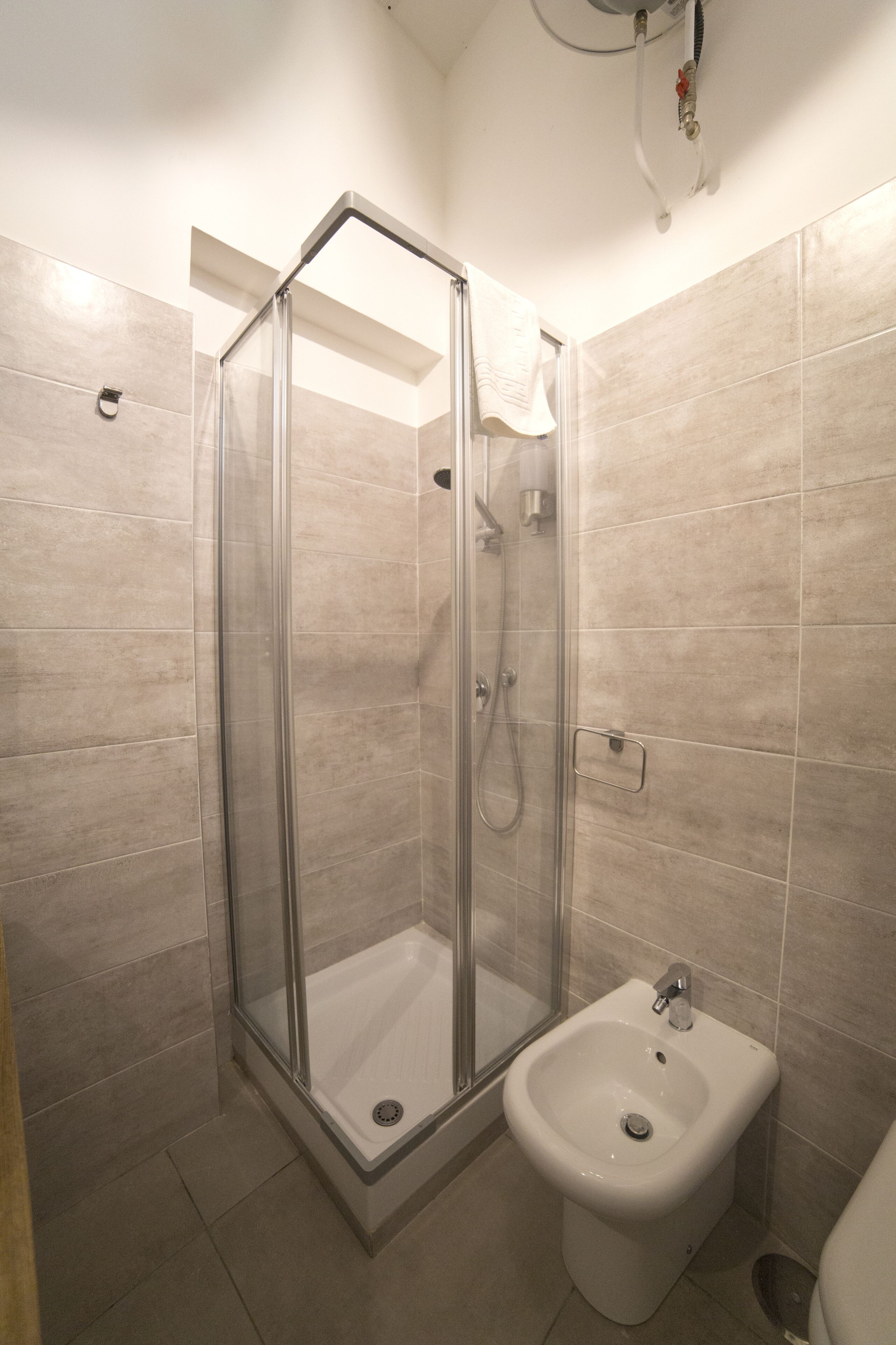 Une salle de bain avec une douche à l’italienne en verre, un lavabo blanc et des carreaux de couleur beige.