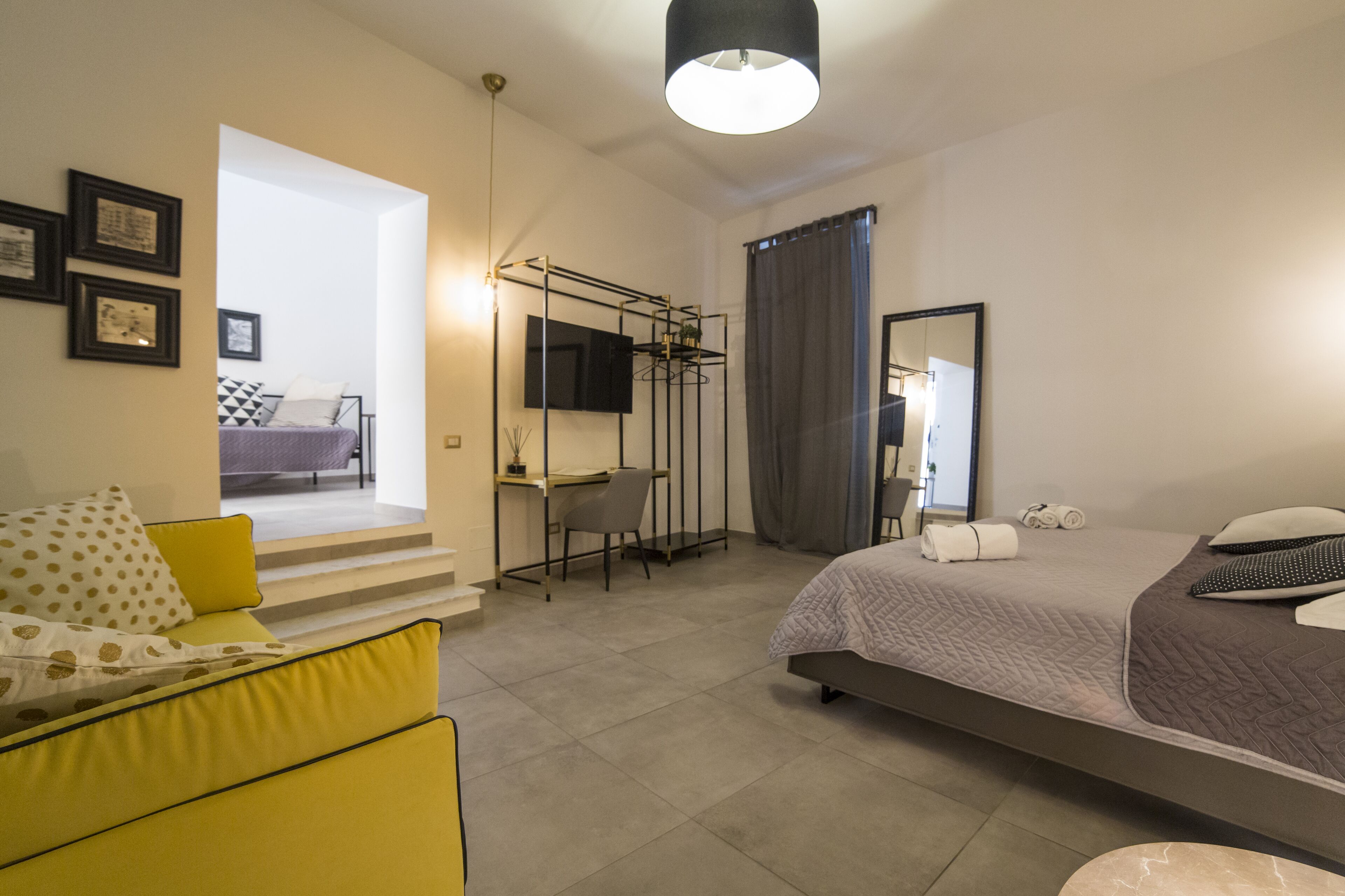 Une chambre d’hôtel moderne avec un lit, un canapé jaune, un bureau et une télévision.