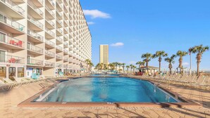 Ein Hotelpoolbereich mit großem Pool, Liegestühlen und Palmen.