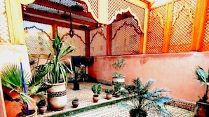 Un patio con suelo de baldosas, plantas en macetas y una valla de madera decorativa.