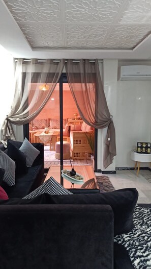 A living room with a black sofa, a glass coffee table, and sheer curtains. - Résidence Harmony (Marrakech)