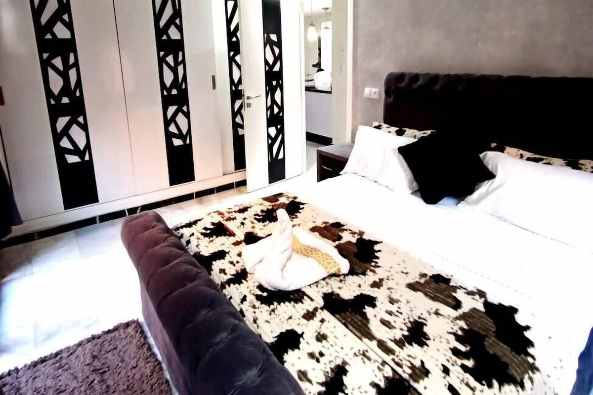 A bedroom with a large bed, a dark-colored sofa, and a patterned rug.