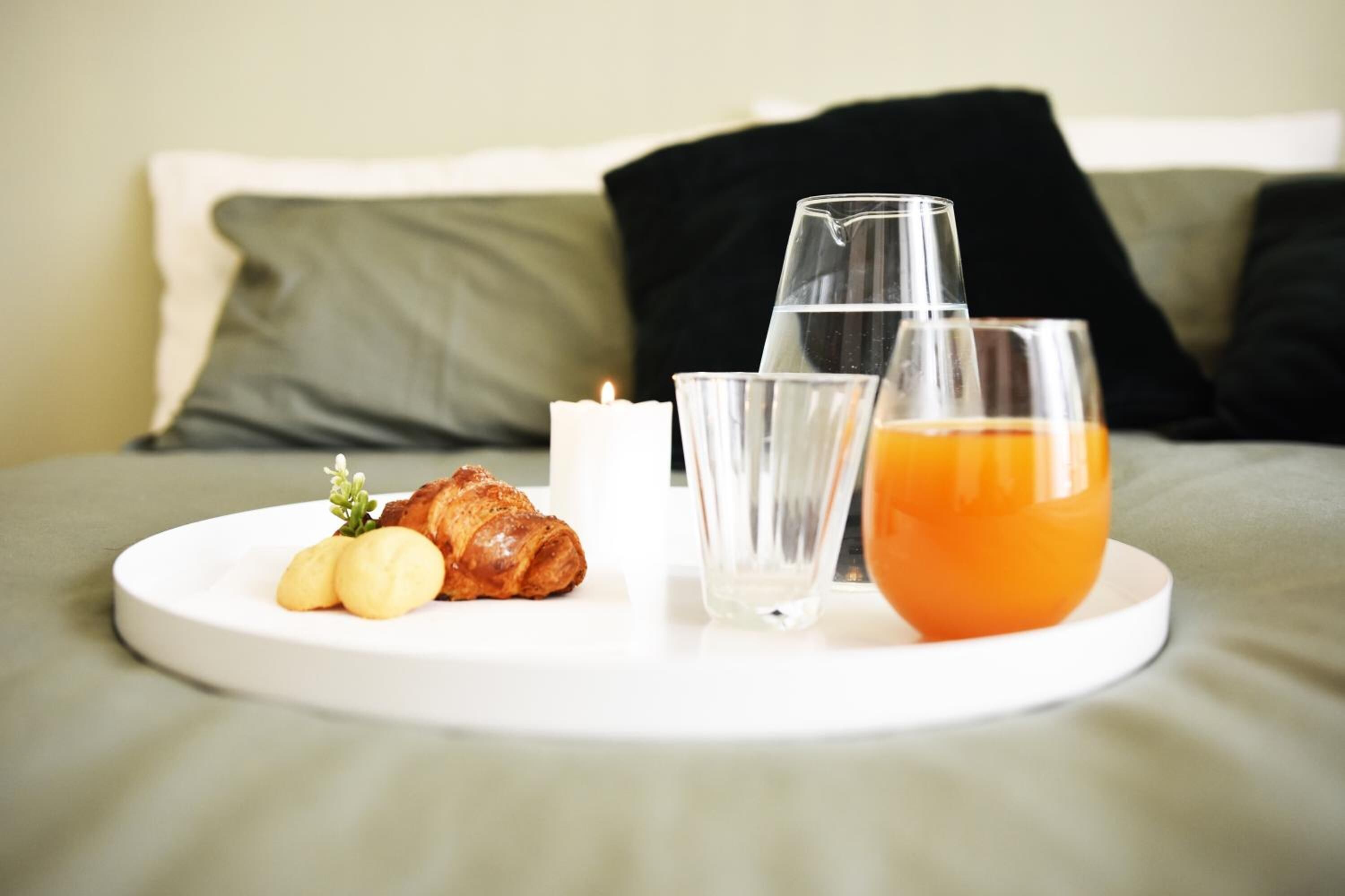 A breakfast tray on a bed with croissants, a glass of orange juice, and a candle.