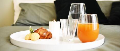 A breakfast tray on a bed with croissants, a glass of orange juice, and a candle.