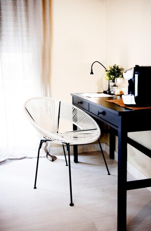 A room with a white woven chair, a dark wooden desk, and a lamp. - Fabrì 171 (Pescara)