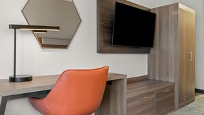 Une chambre moderne avec un bureau en bois, un fauteuil en cuir, un téléviseur fixé au mur et un grand miroir.
