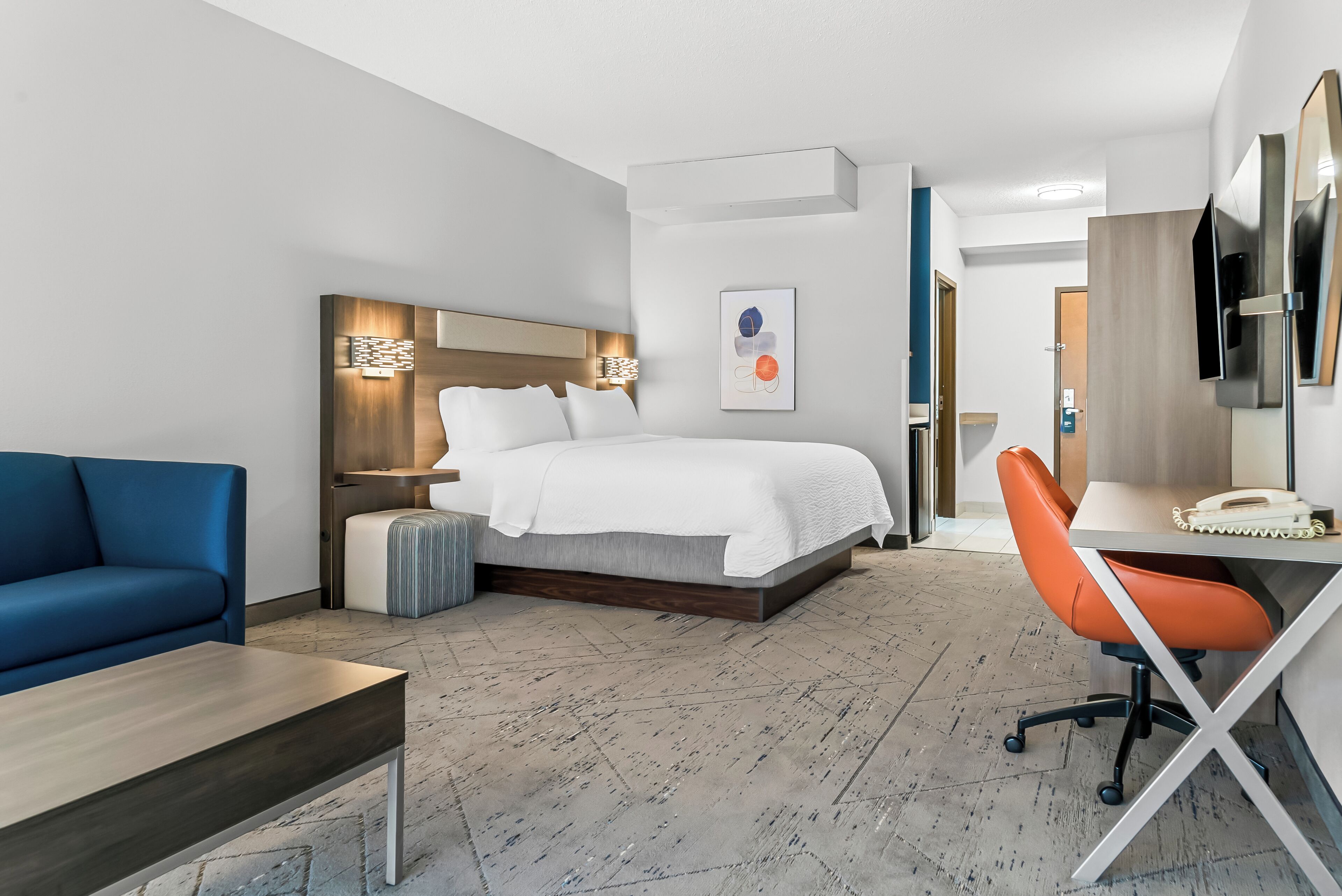 A hotel room with a bed, a desk, a chair, a sofa, and a TV.