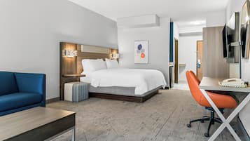 A hotel room with a bed, a desk, a chair, a sofa, and a TV.