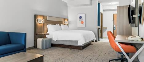 A hotel room with a bed, a desk, a chair, a sofa, and a TV.