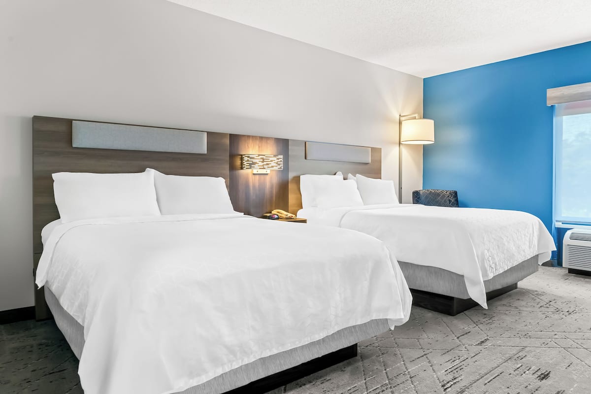 A hotel room with two beds, a modern headboard, a wall-mounted lamp, and a large window.