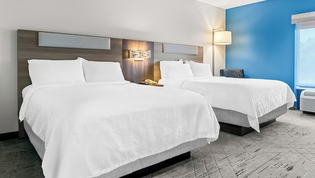 Une chambre d’hôtel avec deux lits, une tête de lit moderne, une lampe fixée au mur et une grande fenêtre.