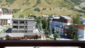 Ein Hotel mit Balkon, im Hintergrund eine Skipiste und eine gebirgige Landschaft.