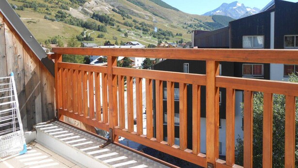 Ein Holzbalkon mit Blick auf eine gebirgige Landschaft und ein Gebäude mit dunkler Fassade.