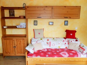Cozy bedroom with a wooden bed, bedspread, and matching headboard, featuring a shelf unit and wardrobe.