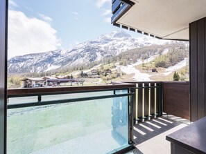 A balcony with a view of a mountain landscape, including snow-capped peaks and a valley with buildings.